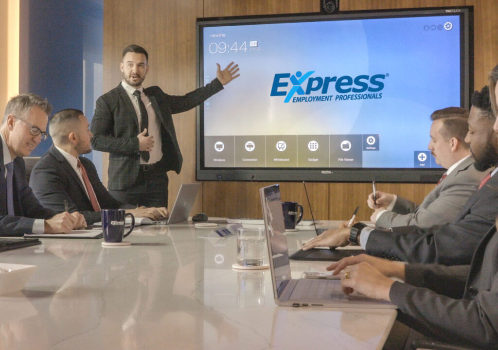 A man pointing to a screen with the Express logo during a meeting